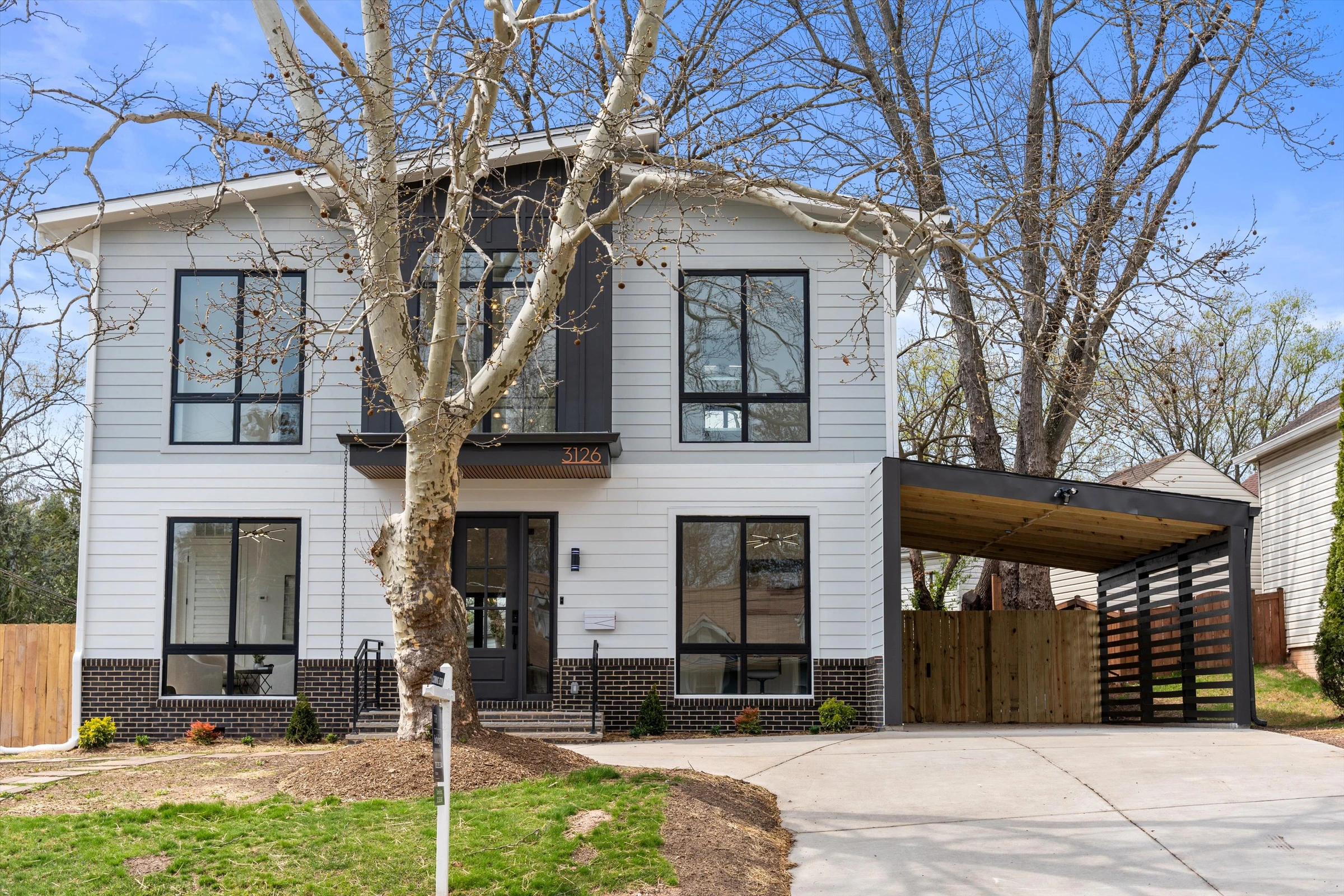 Wide front view of modern new construction at 3126 Westley Rd showing white lap siding, two-story facade, metal carport, and mature trees