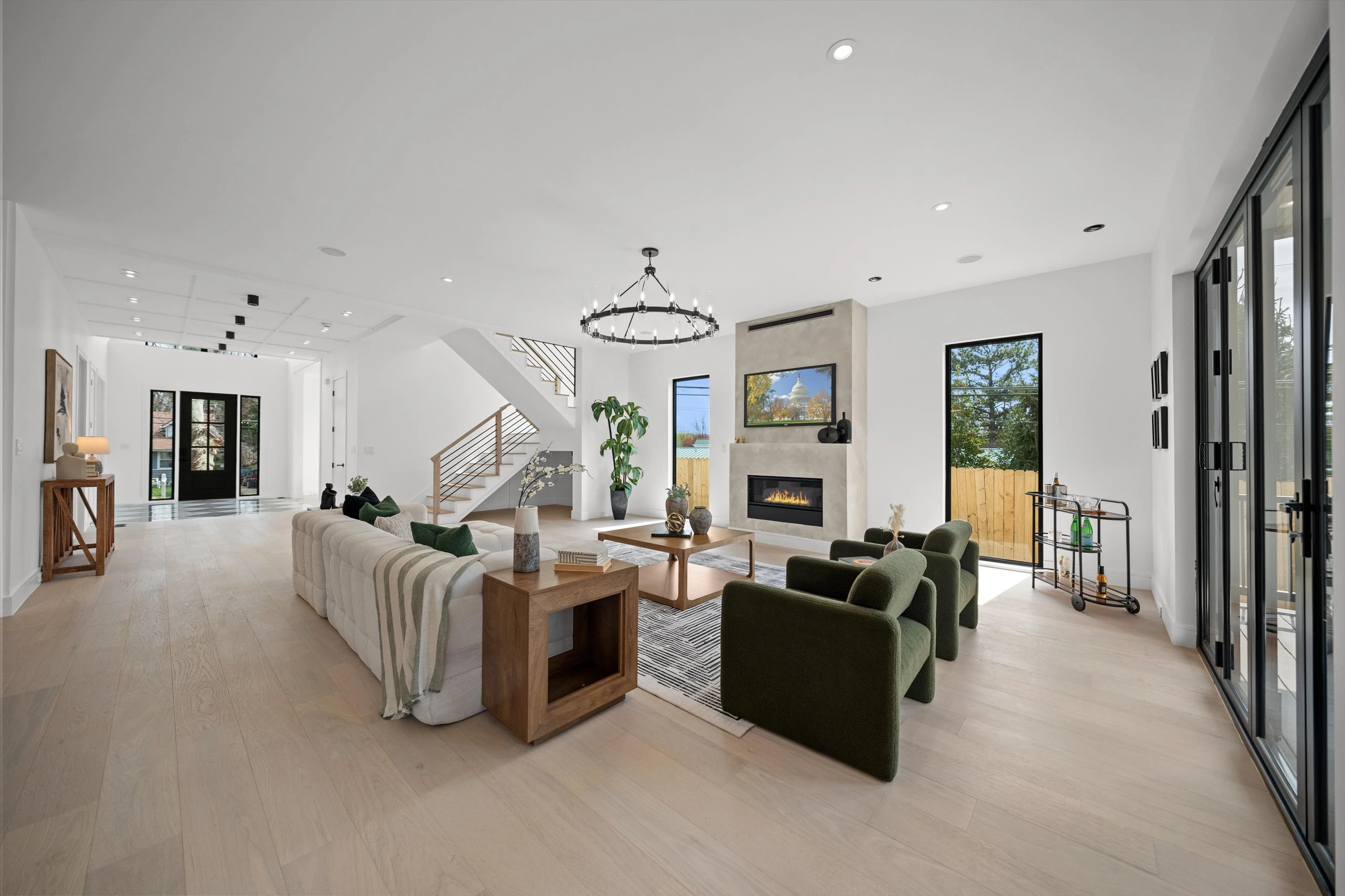 Open-plan family room showing concrete fireplace, modern staircase with horizontal metal railing, sectional sofa, and connection to kitchen