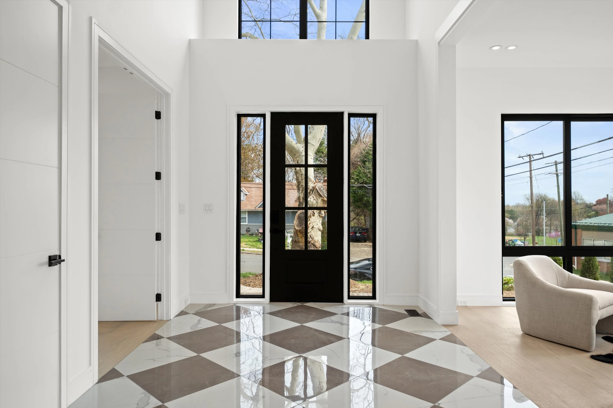 Foyer looking toward black glass-paned front door with transom windows, checkered marble floor, and natural light flooding through sidelights