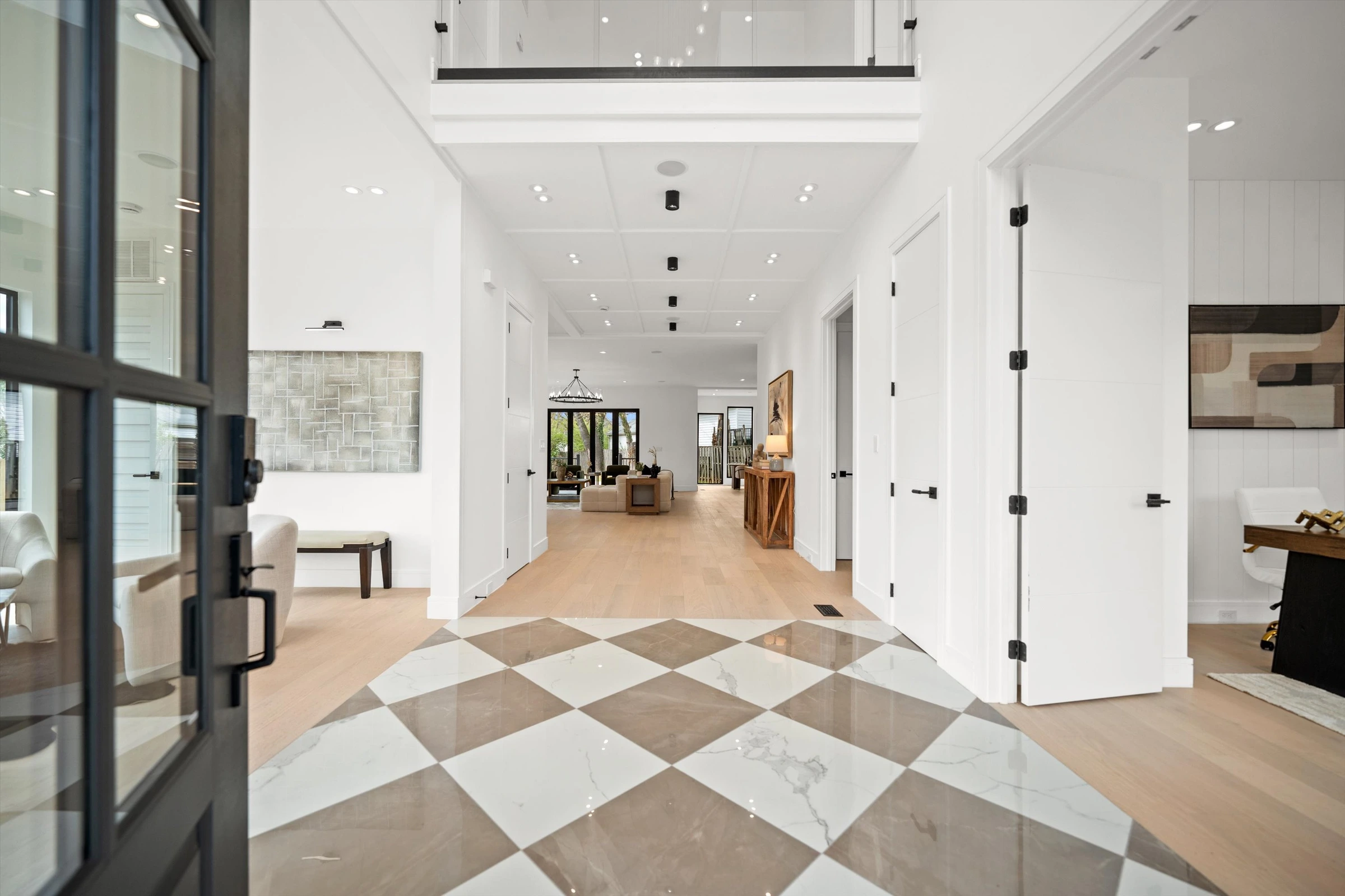 Grand entry foyer with checkered marble floor, double-height ceiling, light oak hardwood floors, and sightline through to living area