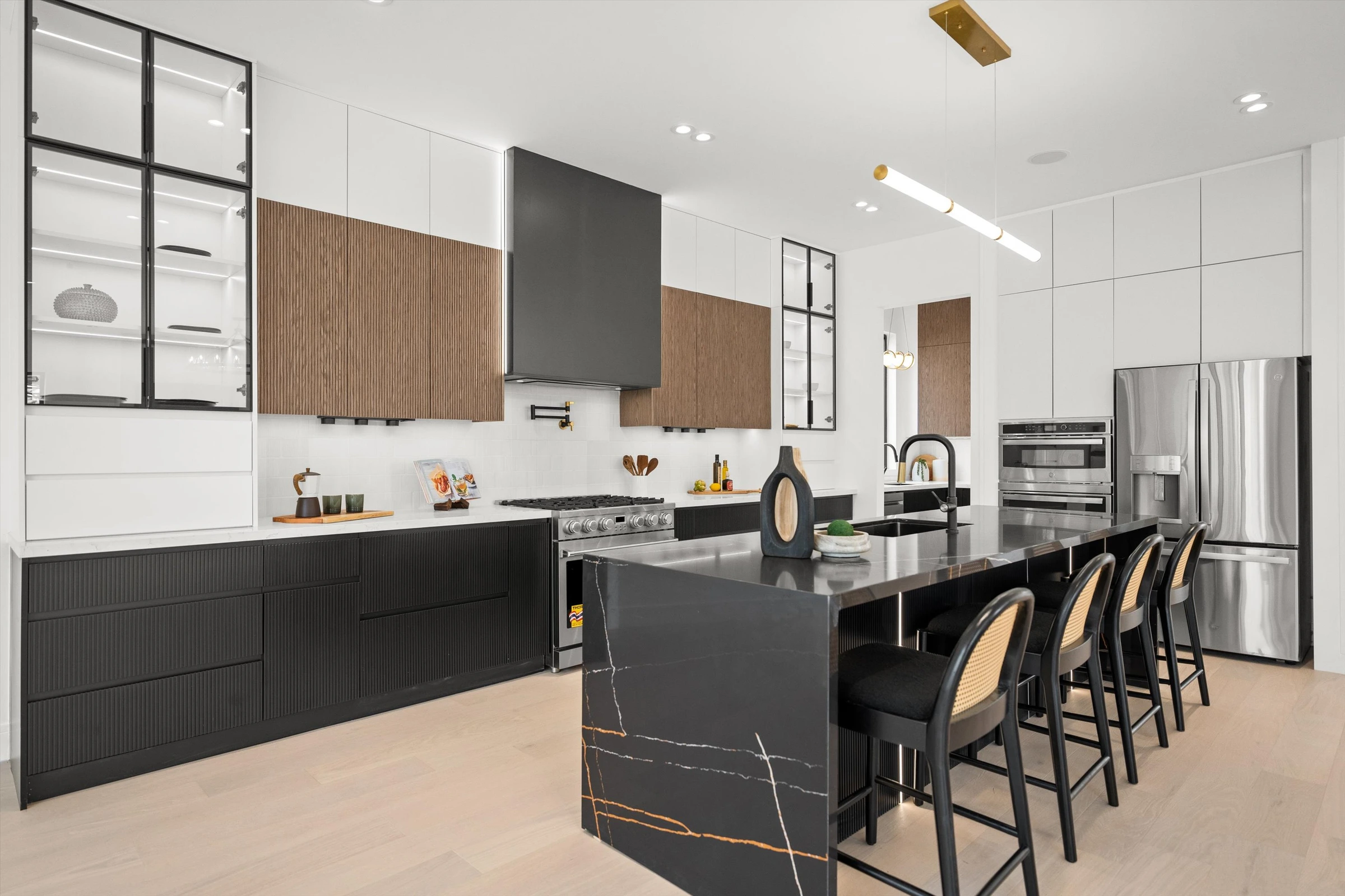 Kitchen view showing black marble island with gold veining, glass-front upper cabinets, wood accent panels, and stainless professional appliances