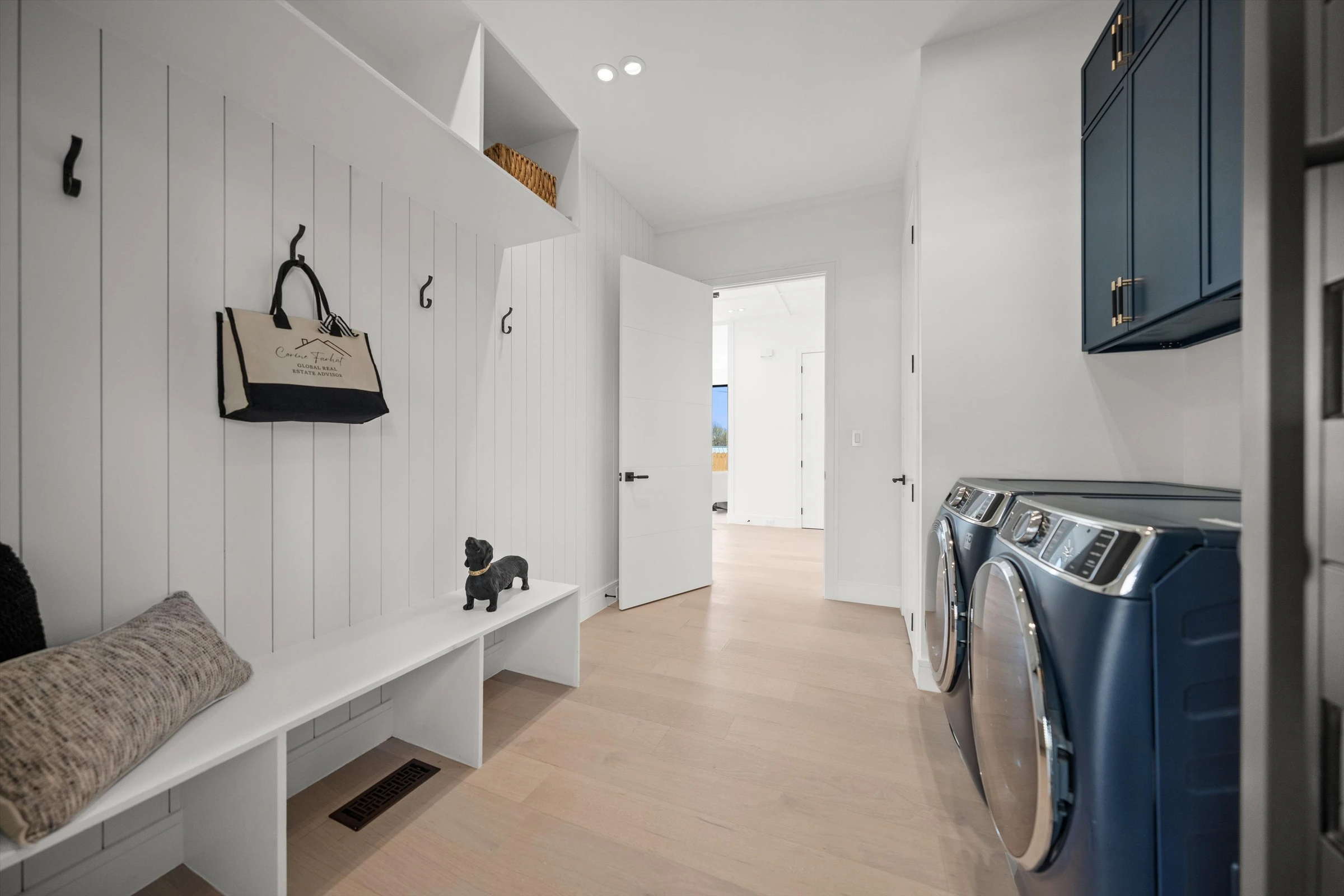 Mudroom and laundry with white shiplap built-in bench, coat hooks, navy blue front-load washer and dryer, and upper storage cabinets