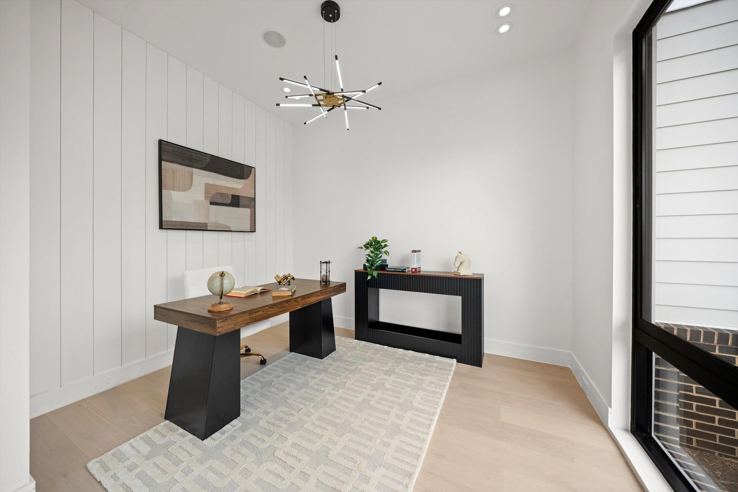 Home office with vertical shiplap accent wall, walnut desk, modern sputnik chandelier, and floor-to-ceiling black-framed window