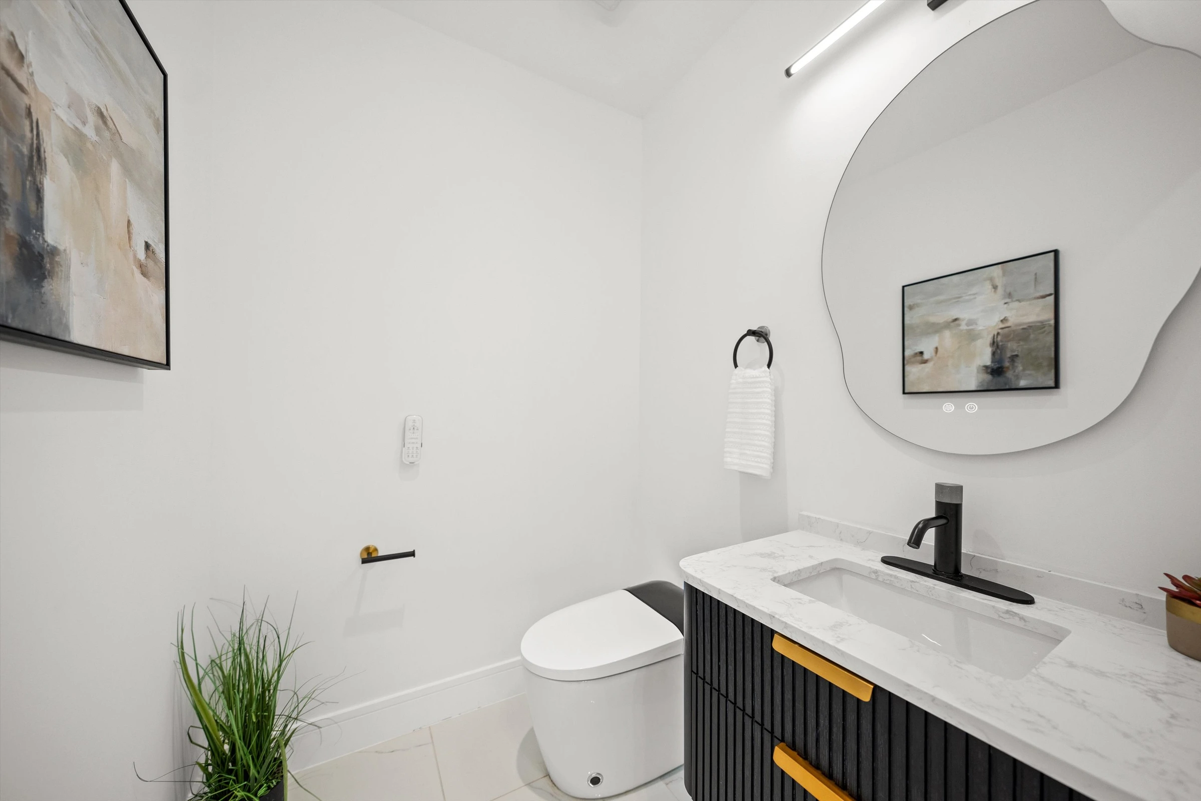 Powder room with organic-shaped mirror, marble countertop, black fluted vanity with gold accents, and abstract artwork