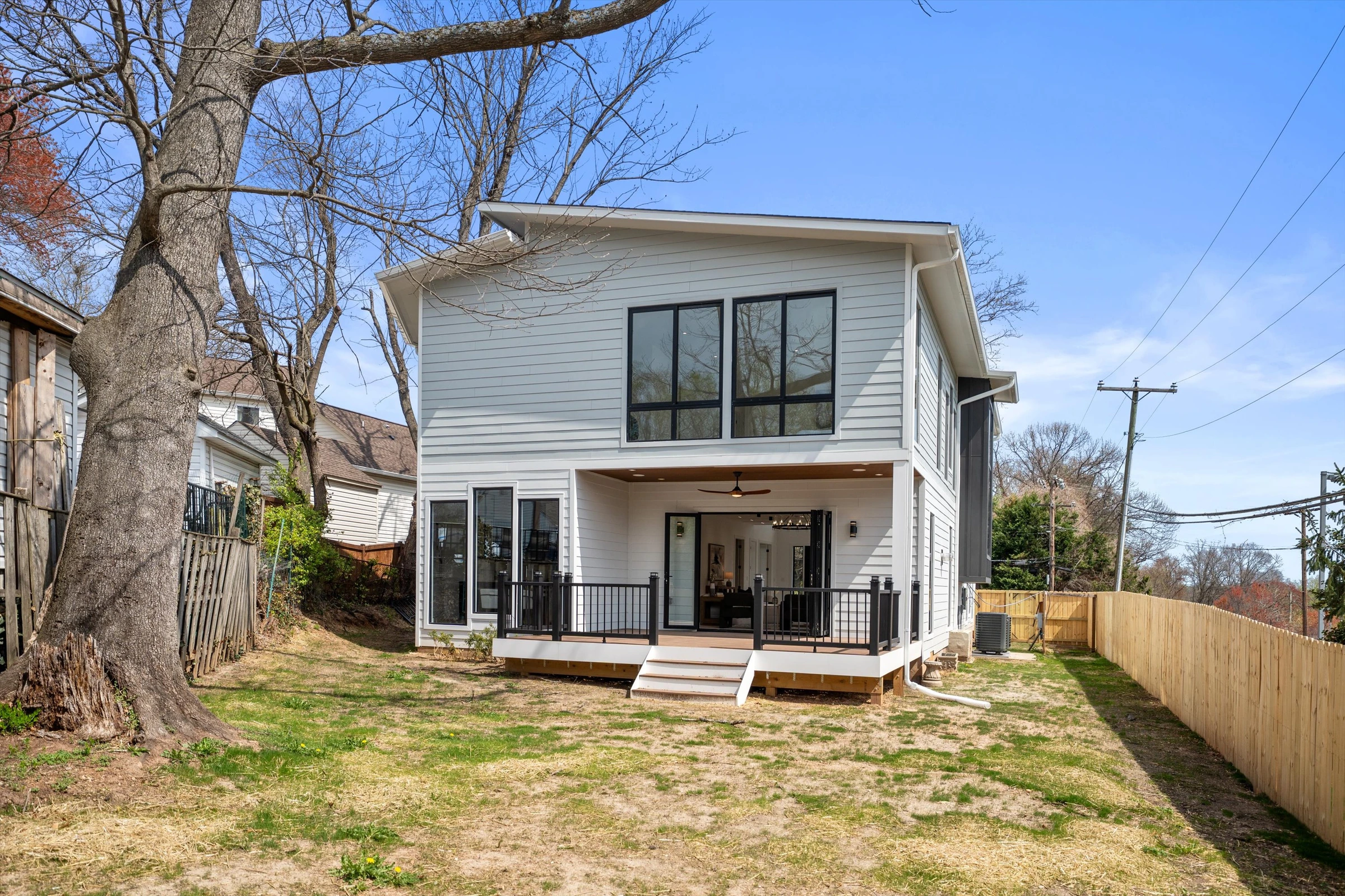 Rear exterior showing covered porch with bi-fold doors, second-floor windows, backyard with mature trees, and wood privacy fence