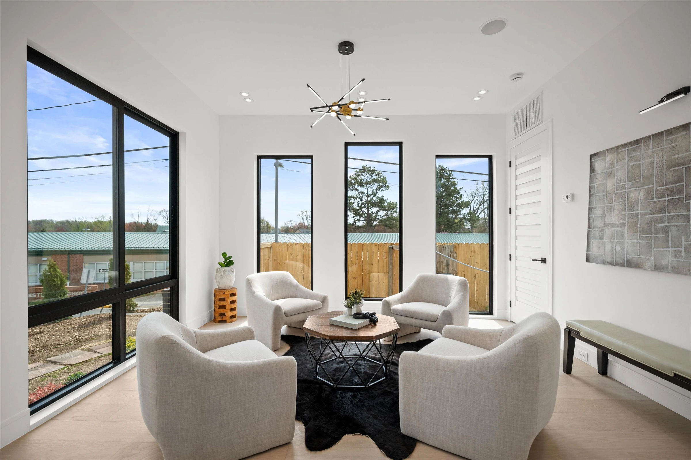 Formal sitting room with four white swivel chairs, round walnut coffee table, sputnik chandelier, and tall black-framed windows